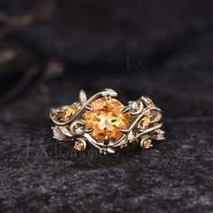 a gold ring with an orange topazte surrounded by leaves and vines on a black surface