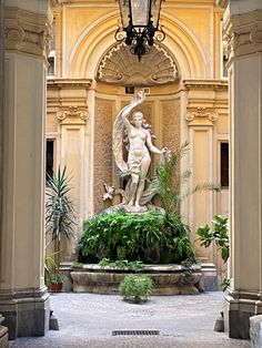 the statue is surrounded by greenery in front of an ornate building with columns and arches