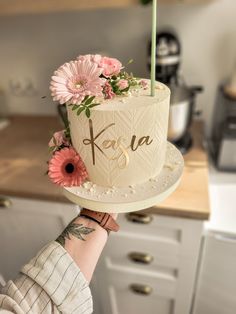 a person holding up a cake with flowers on it and the word kaka written in cursive writing