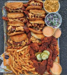 a tray filled with lots of different types of food on top of a table next to bowls of fries and coleslaw