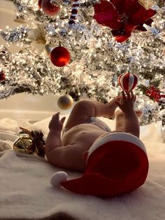 a baby laying on its back in front of a christmas tree with ornaments hanging from it