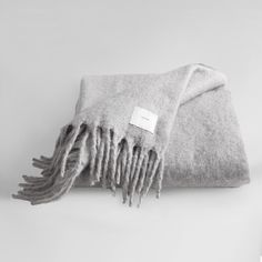 a gray blanket with fringes on it and a white tag hanging from the end