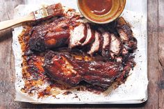 barbecued meat with bbq sauce on a wooden table next to a small bowl of dipping sauce