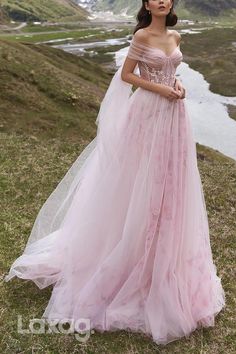 a woman in a pink dress standing on the side of a hill with mountains behind her