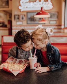 two young children sitting at a table with food and drinks