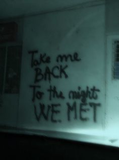 graffiti written on the side of a wall in a dark room with window and blinds