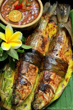 grilled fish and vegetables on a banana leaf with dipping sauce in a bowl next to it