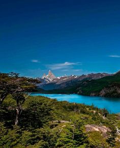 a lake surrounded by trees and mountains under a blue sky