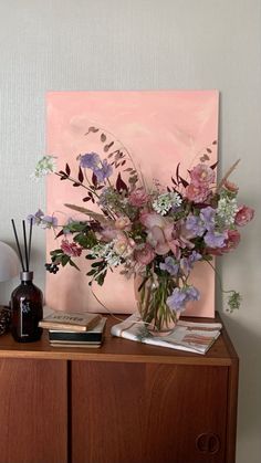 a vase filled with lots of flowers on top of a wooden table next to a painting