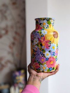 a woman holding up a colorful vase with flowers painted on it's bottom and sides