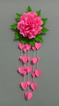 pink paper flowers and green leaves are hanging from the side of a wall with sticks