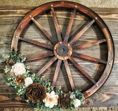 an old wagon wheel with flowers and greenery on the rim is mounted on a wooden wall