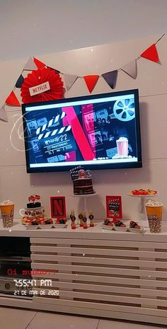 a large screen tv mounted to the wall above a buffet table filled with cupcakes