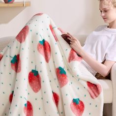 a woman sitting on a couch under a white blanket with red cherries printed on it