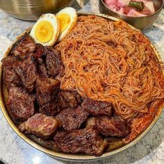 a plate with noodles, meat and an egg on it sitting on a table next to other dishes