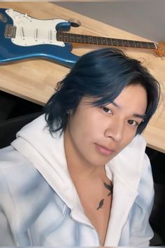 a young man with blue hair sitting in front of a guitar and looking at the camera