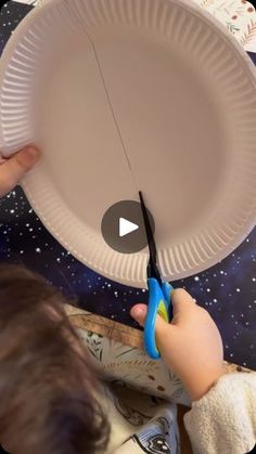 a person cutting paper with scissors on top of a table next to a space theme