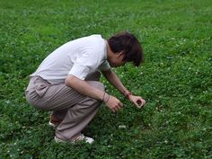 a woman kneeling down in the grass with her hand on a small bird's head