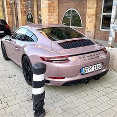 a pink porsche parked next to a black and white striped pole in front of a building