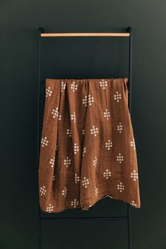 a brown and white patterned towel hanging on a clothes rack in front of a black wall