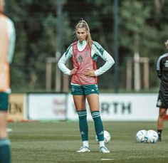 a woman standing on top of a soccer field with her hands on her hips as she looks at the ball