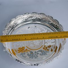 a measuring tape is in front of a silver plate with floral designs on it and a yellow ribbon around the edge