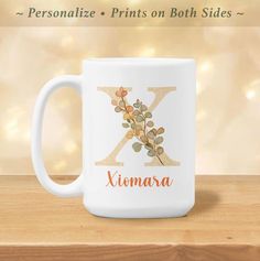 a white coffee mug with the letter k on it and an orange floral design is sitting on a wooden table