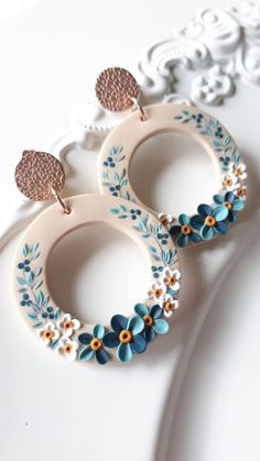 two white and blue flower hoop earrings on top of a table next to a lace doily