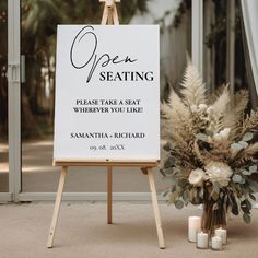 an open seating sign sitting next to a vase with flowers and candles on the floor