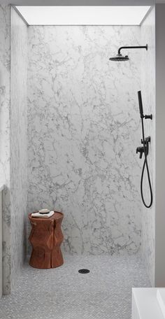 a bathroom with marble walls and flooring in the shower area, along with a wooden stool