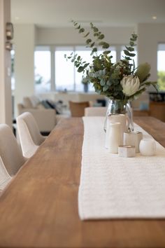 a wooden table topped with white chairs and a vase filled with flowers on top of it