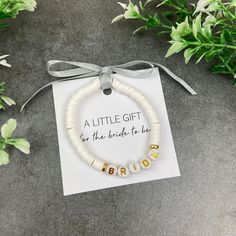 a little gift for the bride to be beaded bracelet on a card next to flowers