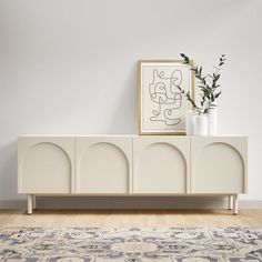 a white cabinet sitting on top of a wooden floor next to a rug and potted plant