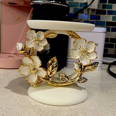 a gold and white flower brooch sitting on top of a counter next to a blender