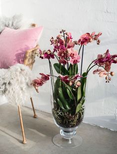 a glass vase filled with pink flowers sitting on top of a table next to a chair