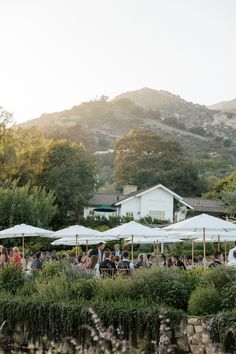 a group of people sitting at tables under umbrellas in front of a mountain range