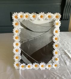 a white frame with yellow and white flowers in the shape of a flower on it