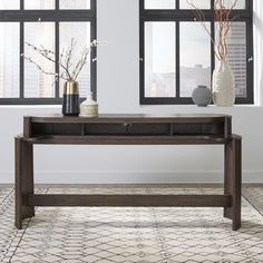 a wooden table with two vases on it in front of large windows and a rug