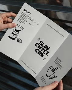 two hands holding open menus in front of a metal grate that says slow coffee club