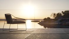 a chair sitting on top of a cement floor next to a body of water at sunset