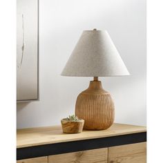 a table lamp sitting on top of a wooden dresser next to a potted plant