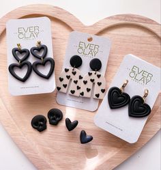 three pairs of heart shaped earrings sitting on top of a wooden tray next to each other