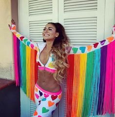 a woman with long hair wearing colorful clothing and holding her arms up in the air