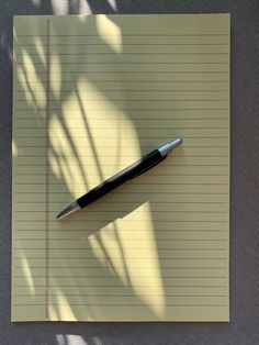 a pen sitting on top of a piece of lined paper next to a shadow of a plant