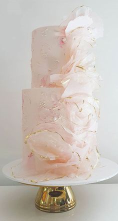 a three tiered cake with pink frosting and gold decorations on a white plate