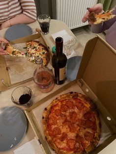 two people sitting at a table eating pizza and drinking wine