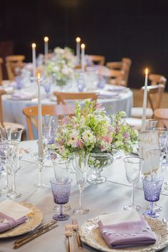 the table is set with purple and white dishes, silverware, and flowers in vases