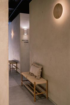 a bench sitting next to a wall with a light on it's side and two chairs in the background