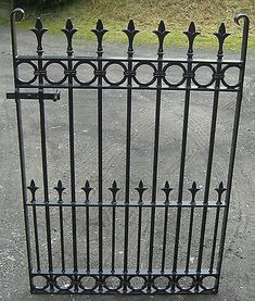 an iron gate on the side of a road with grass and bushes in the background