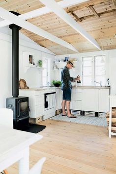 a woman standing in a kitchen next to an open stove top oven and wooden ceiling